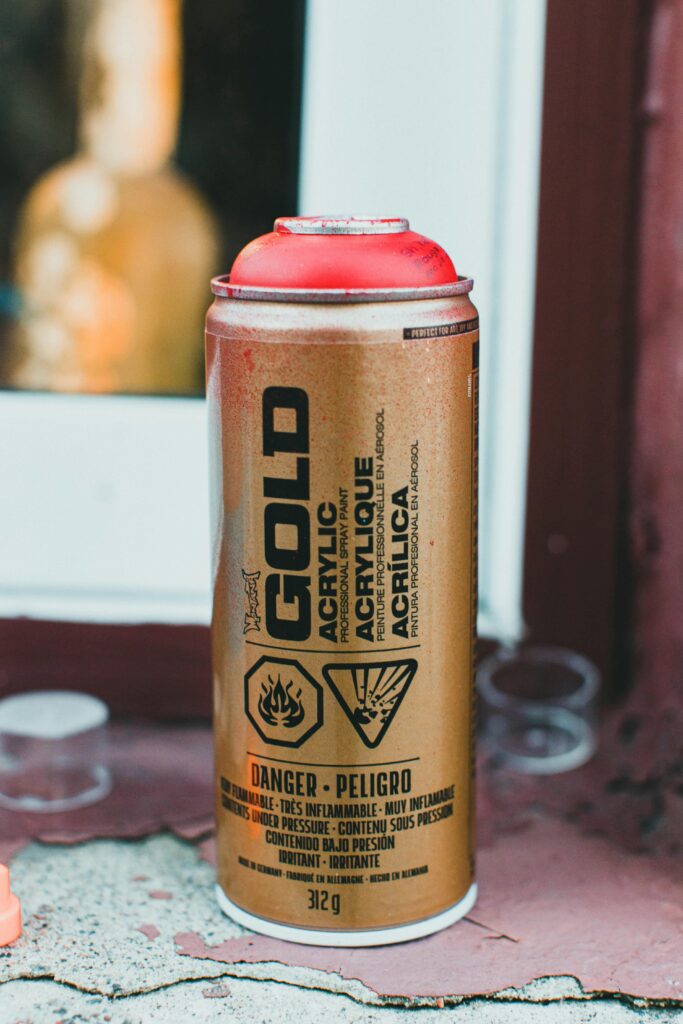 Close-up of a gold acrylic spray paint can on a ledge outdoors.