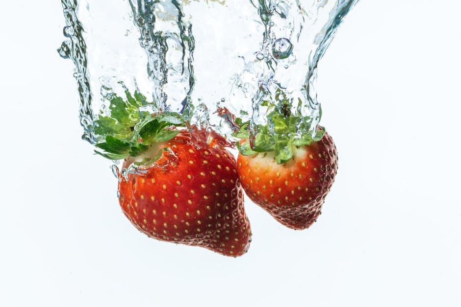 Two ripe strawberries splashing into clear water, isolated on white.